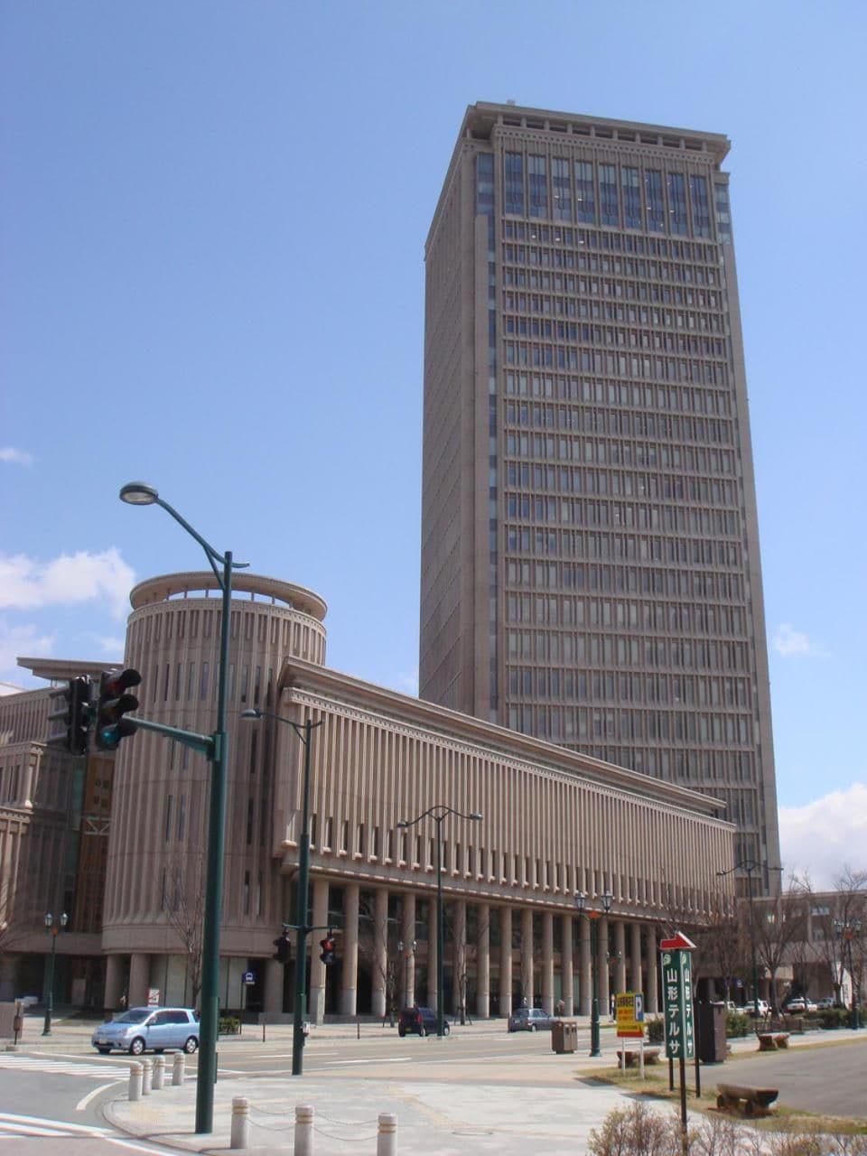 A tall building with a modern design, a street with traffic lights, and a clear blue sky.