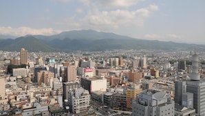 A cityscape with a mix of modern and traditional buildings, a prominent tower, and a mountain range in the background. - Yamagata Eki Nishiguchi Washington Hotel (Yamagata)