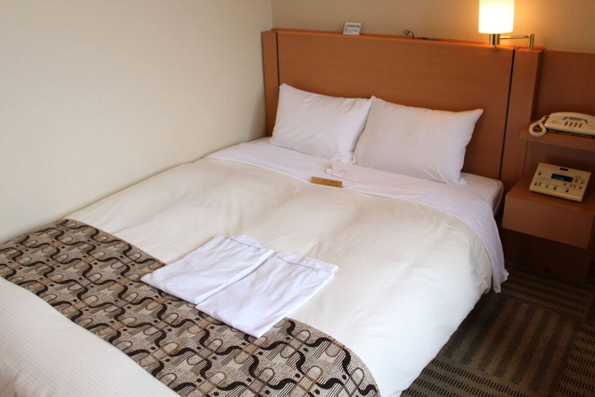 Habitación de hotel con una cama, una mesita de noche con teléfono y cabecera.