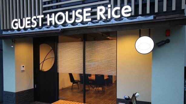A restaurant named "GUEST HOUSE Rice" with a wooden bench outside, a black door, and a visible interior with tables and chairs.