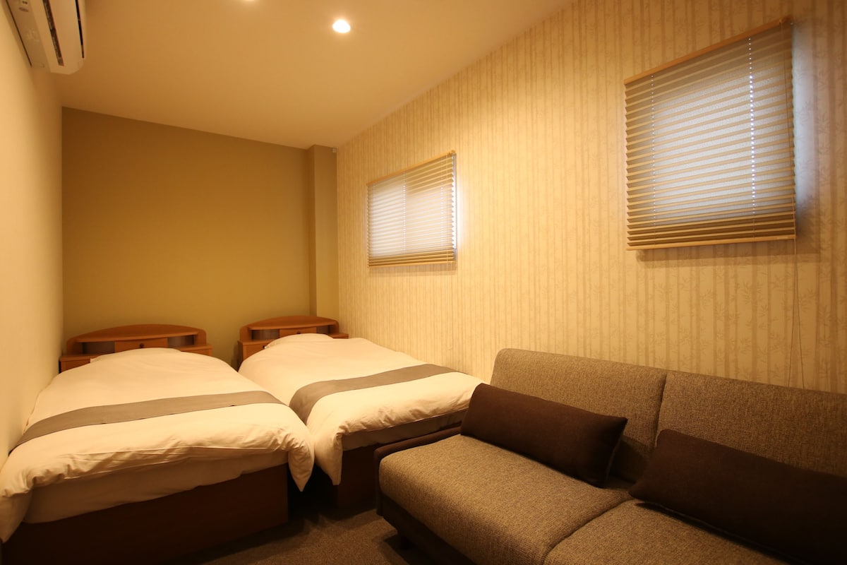 Ein Schlafzimmer mit zwei Einzelbetten, einem Schlafsofa und einem Fenster mit Jalousien.