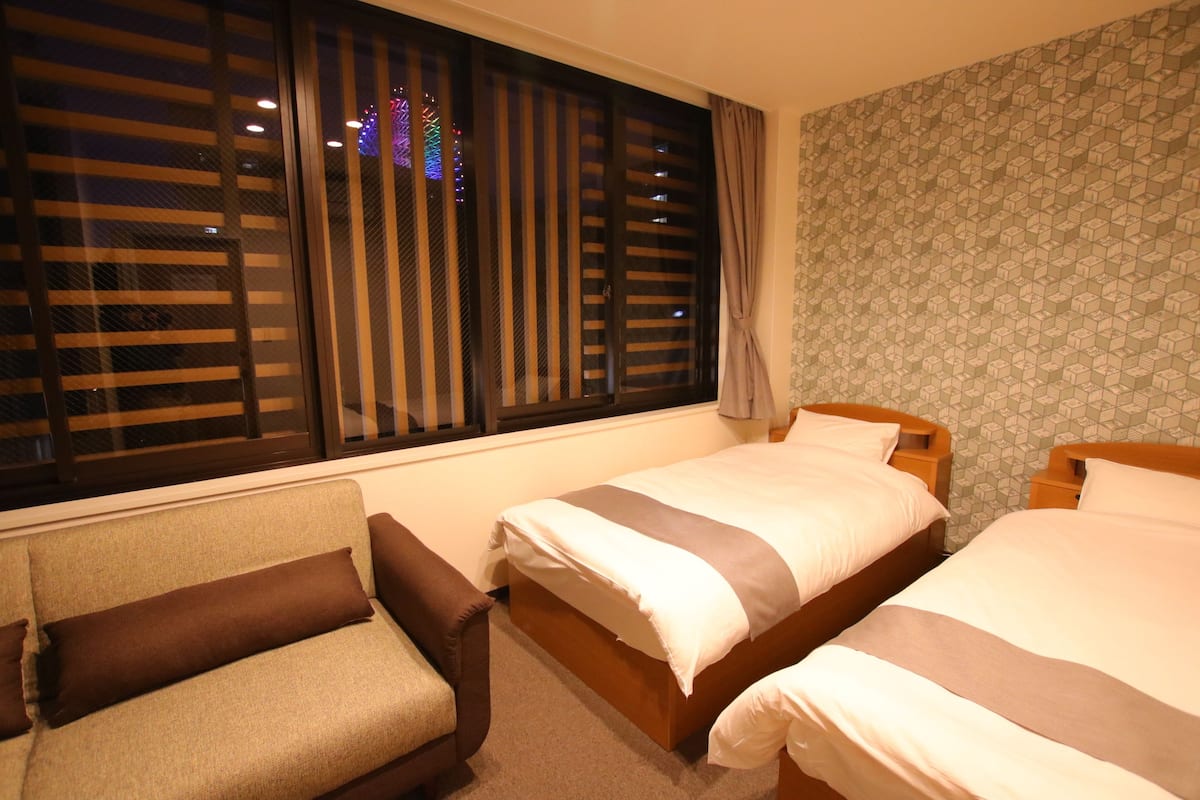 Ein Hotelzimmer mit zwei Einzelbetten, einem Sofa und einem Fenster mit Jalousien.