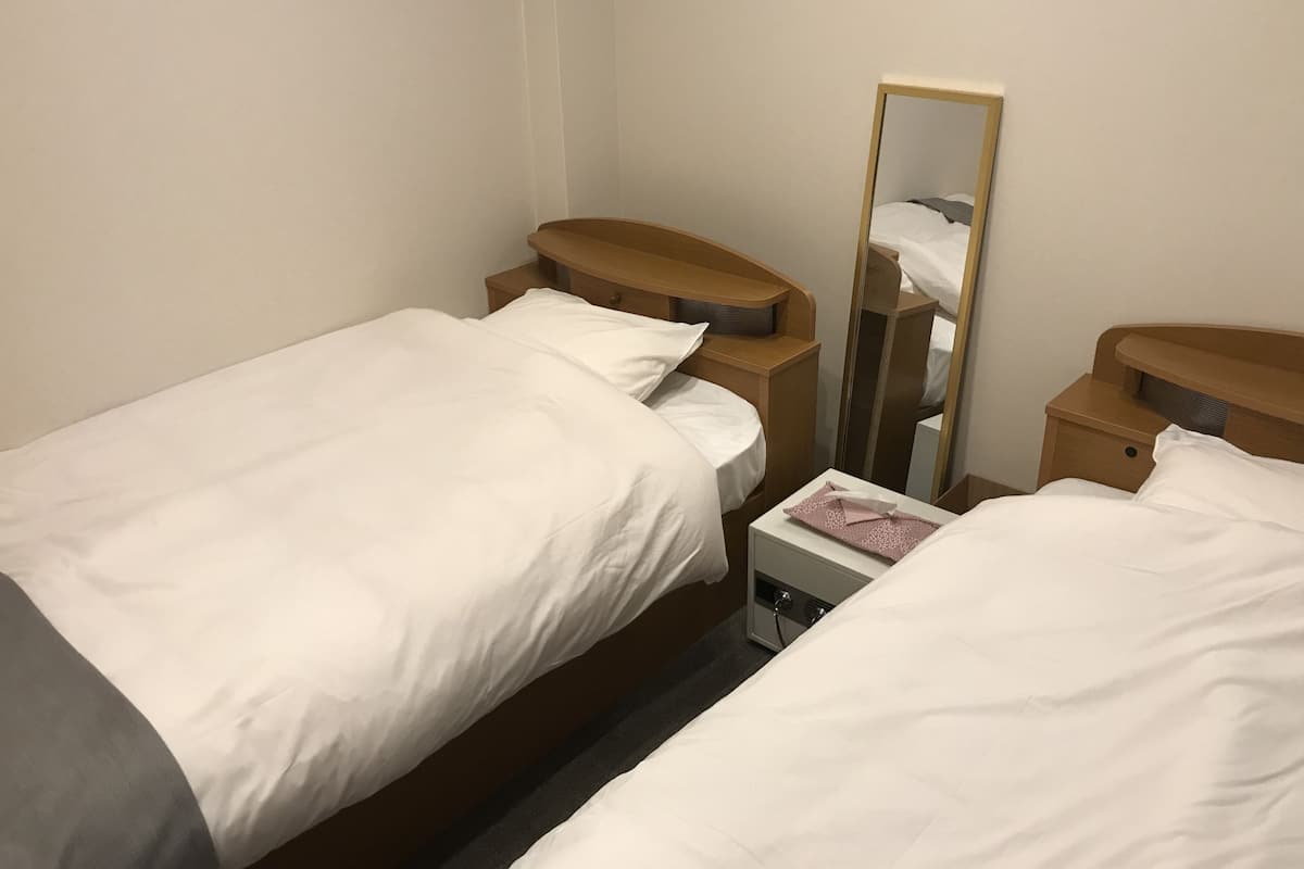 Ein Hotelzimmer mit zwei Einzelbetten, einem Nachttisch mit Lampe, einem Spiegel und einer kleinen Kommode.