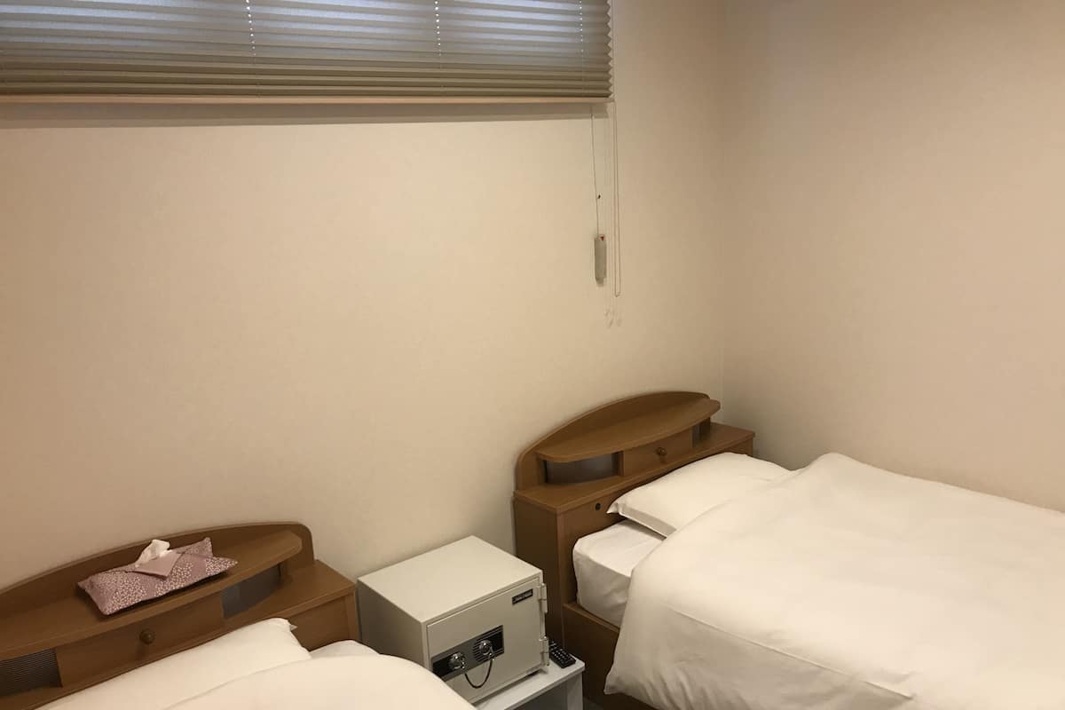 Ein Hotelzimmer mit zwei Einzelbetten, einem Nachttisch mit Lampe und einem kleinen Nachttisch mit Taschentuchbox.