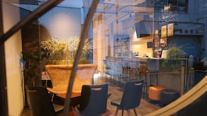 Un restaurante con pared de vidrio, mesas al aire libre y un letrero dando la bienvenida a los clientes.