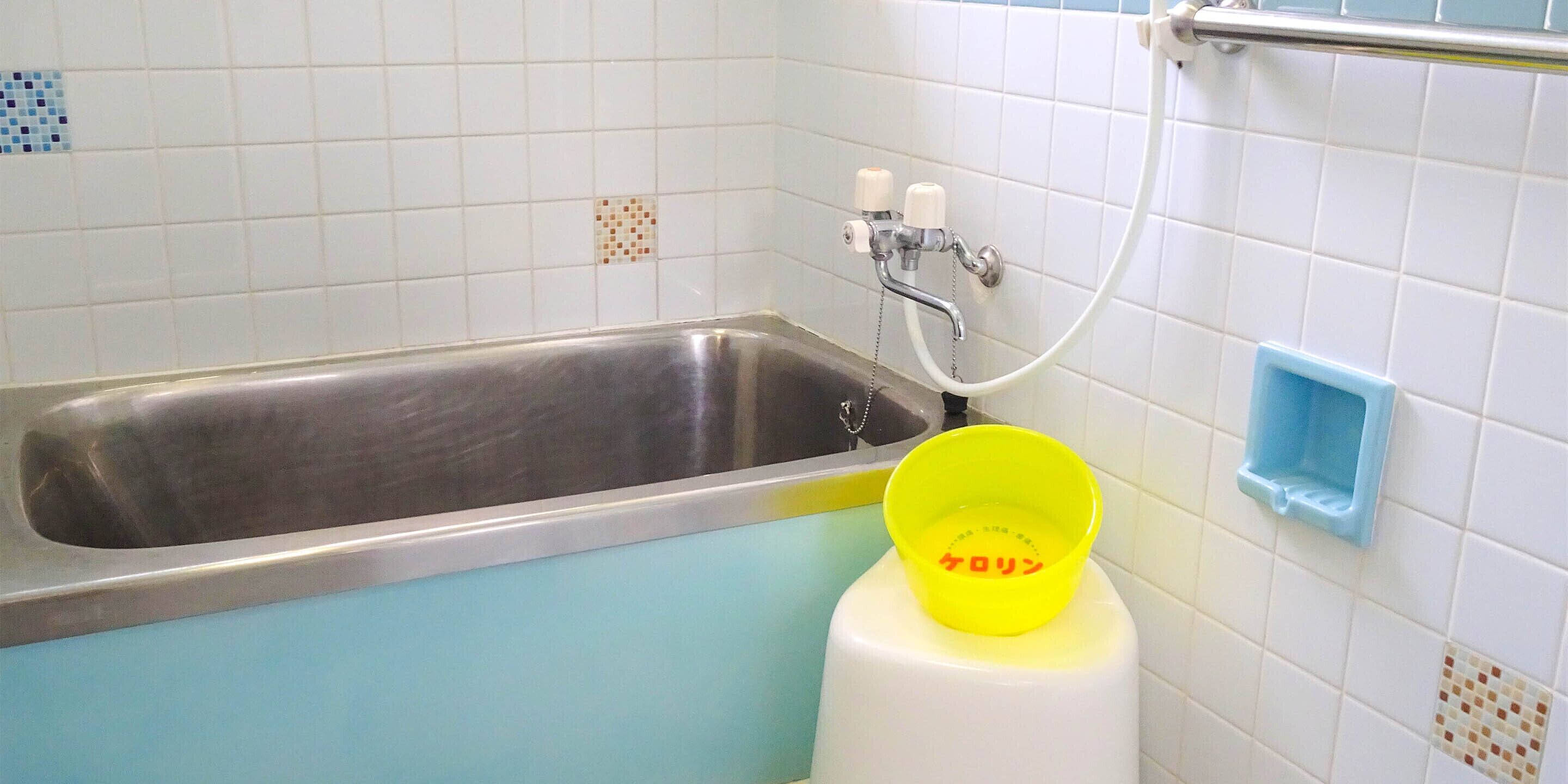 Un baño con bañera, lavamanos y un lavabo amarillo con texto japonés.
