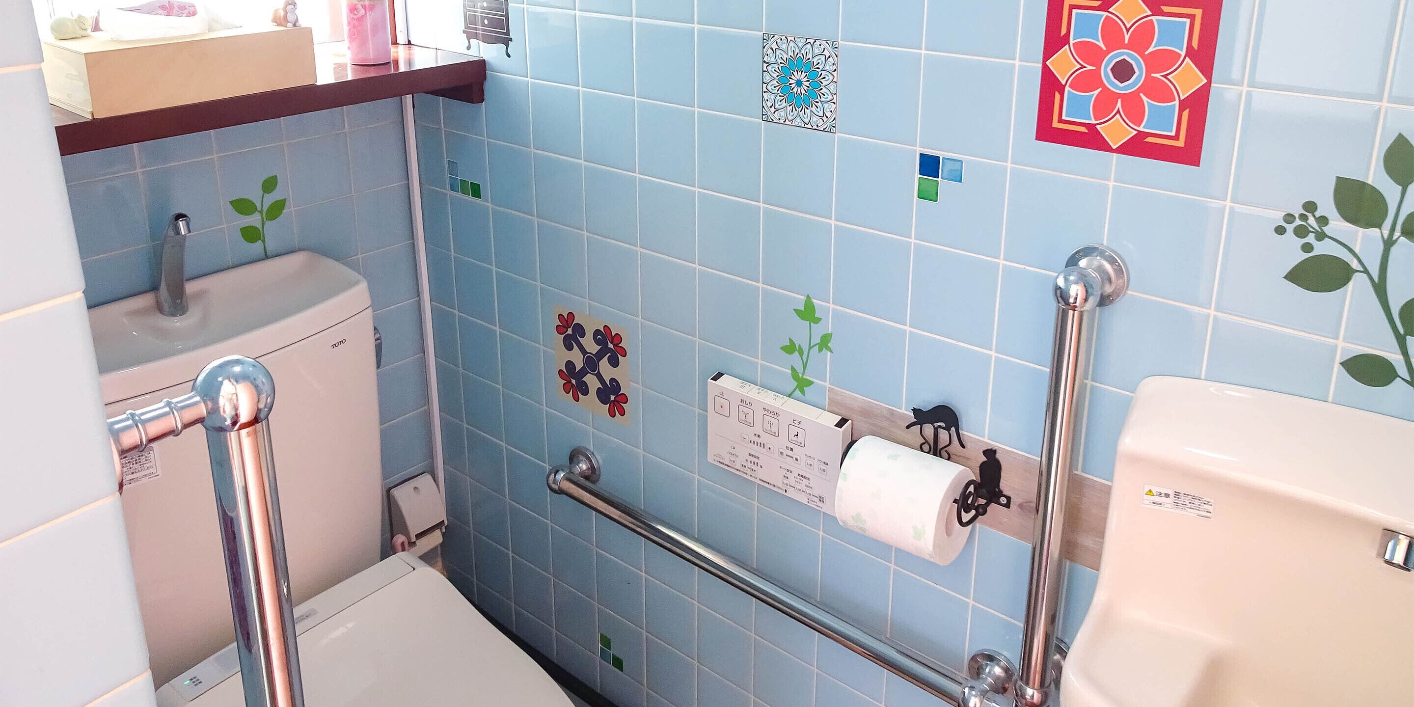 A bathroom with blue tiles, a toilet, a sink, a handrail, and a towel dispenser.