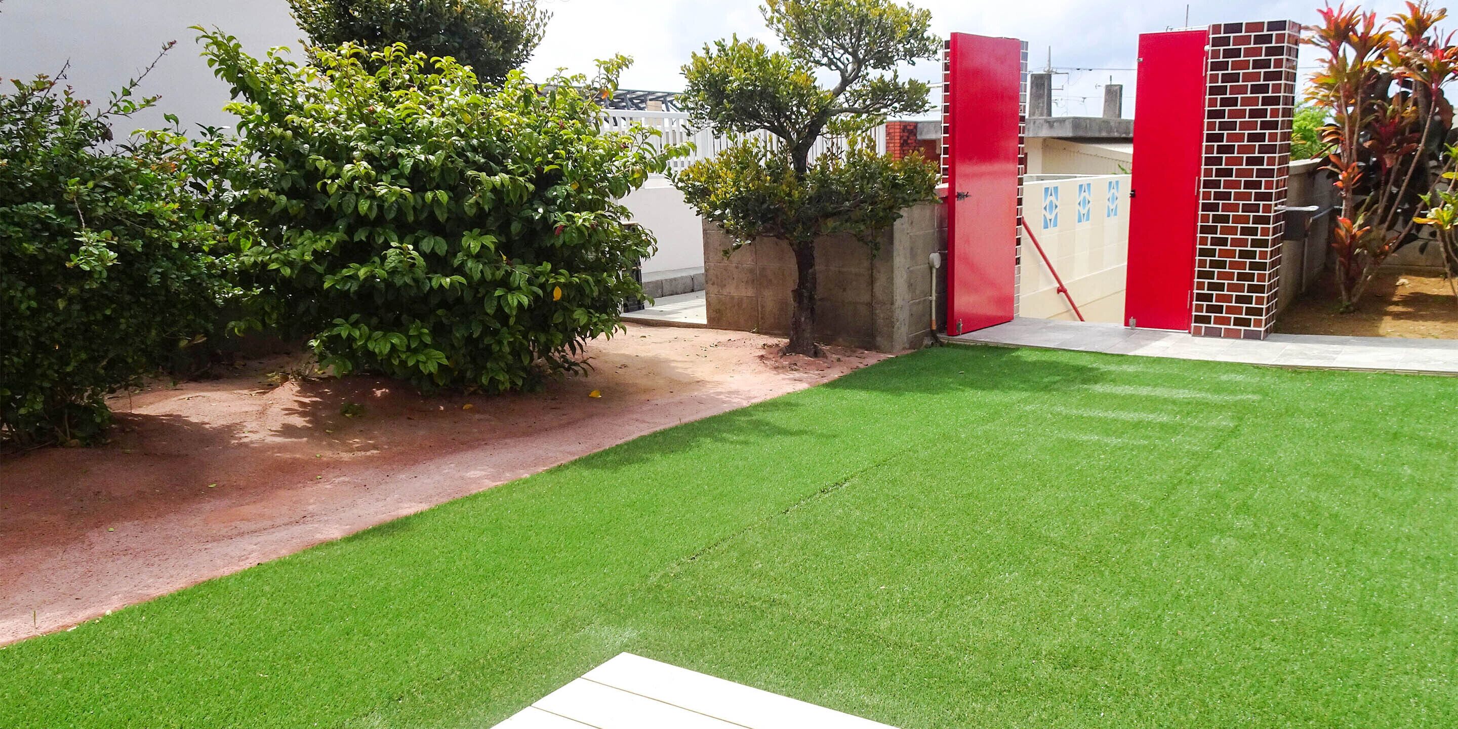 A well-maintained lawn with a red gate and a brick wall.
