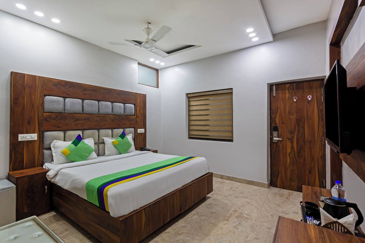 A bedroom with a wooden headboard, a bed with a white and green striped bedspread, a ceiling fan, and a small window with blinds.