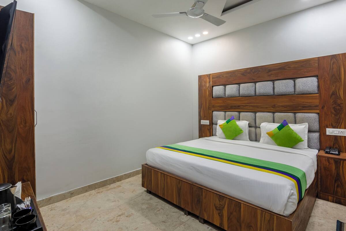 A bedroom with a wooden headboard, a bed with white bedding and colorful pillows, a bedside table with a phone, and a ceiling fan.
