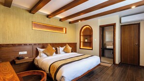 Habitación de hotel con una cama grande, cabecera de madera, una mesita de noche, un escritorio y un baño con espejo y lavamanos.