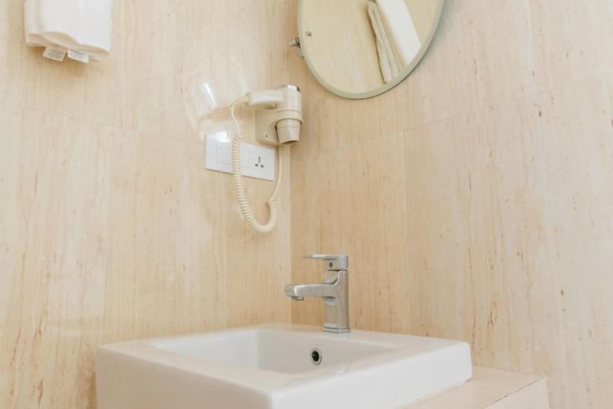 Un baño con un lavabo blanco, un espejo redondo y un teléfono blanco sujeto a la pared.