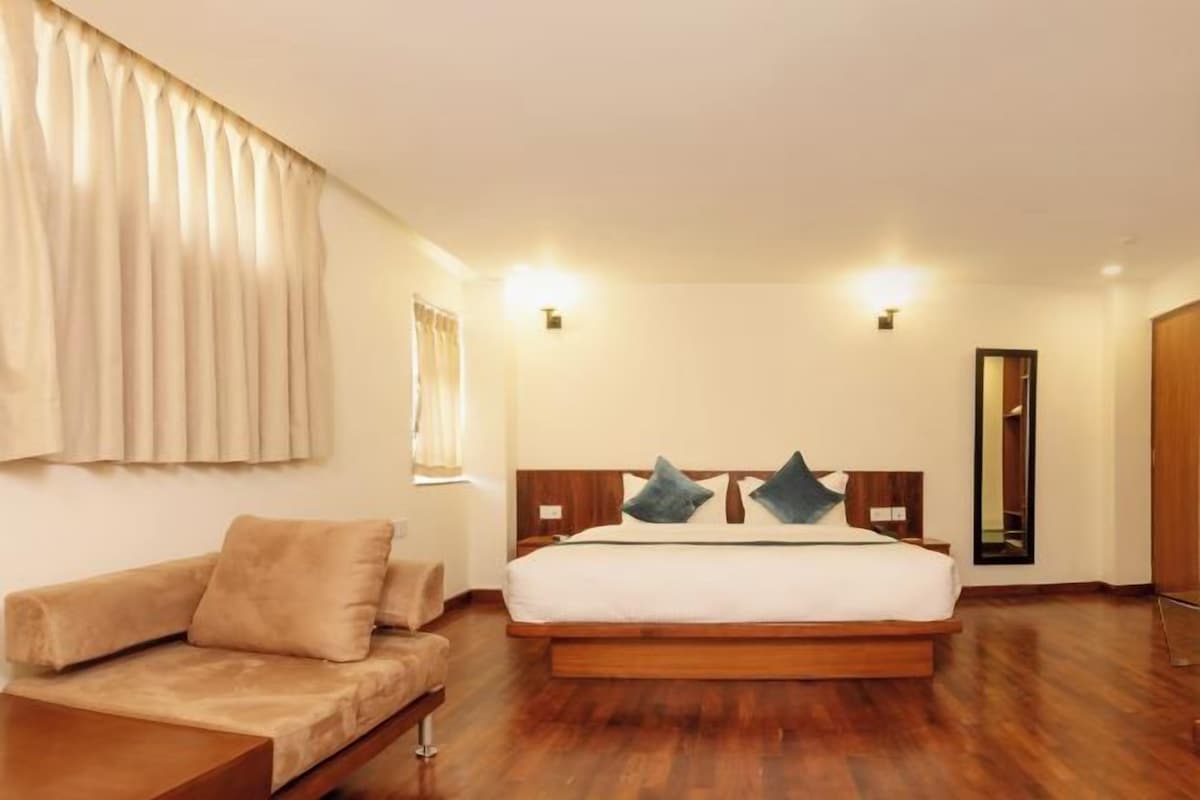 Habitación de hotel con una cama grande, un sofá, piso de madera y un espejo en la pared.