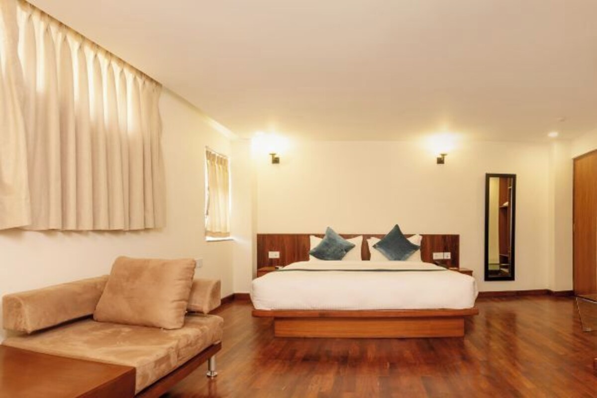 A hotel room with a bed, a sofa, a mirror, and wooden flooring.