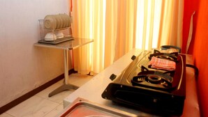 A kitchen with a gas stove, a small table with a kettle, and a window with curtains. - D'Java Homestay Unit Ambarrukmo 2 By The Grand Java (Depok)