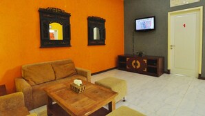 A living room with a sofa, a wooden coffee table, two wall-mounted mirrors, a television, and a cabinet. - D'Java Homestay Unit Ambarrukmo 2 By The Grand Java (Depok)