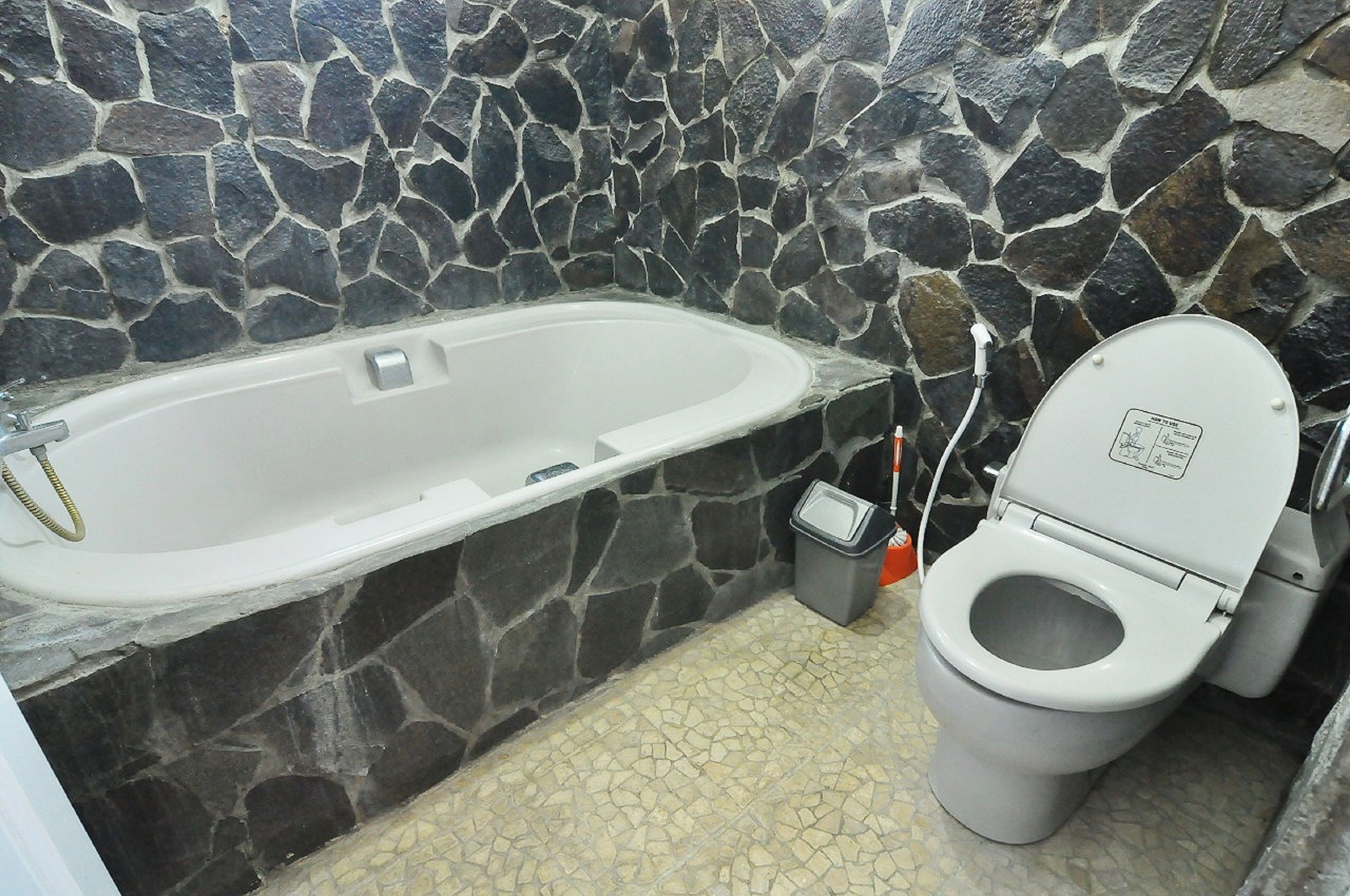 Een badkamer met een stenen muur, een badkuip en een toilet.