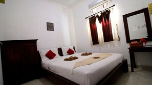 A hotel room with a bed, a wooden wardrobe, a desk with a mirror, and a window with curtains.