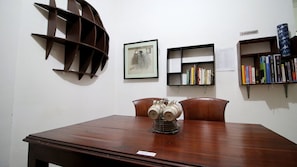 A wooden table with a metal object on it, a framed picture, a bookshelf with books, and a decorative metal shelf.