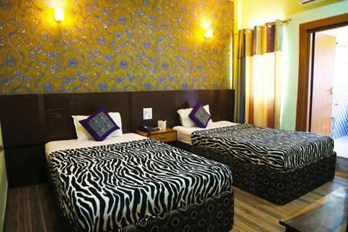 A hotel room with two beds, patterned headboards, and a floral wallpaper.