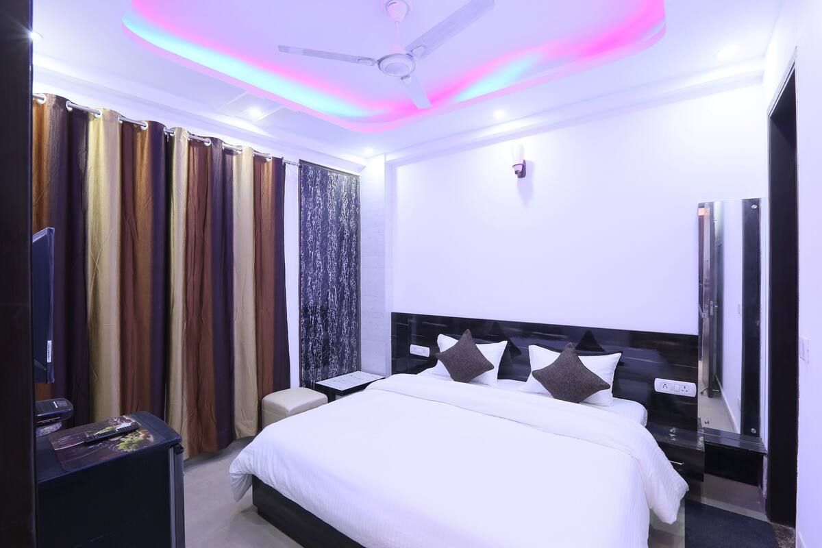 A hotel room with a bed, a nightstand, a TV, curtains, and a ceiling fan.