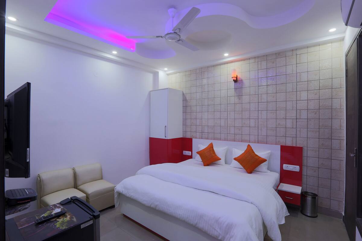 A hotel room with a bed, a TV, a desk, a chair, a ceiling fan, and a wall-mounted light.