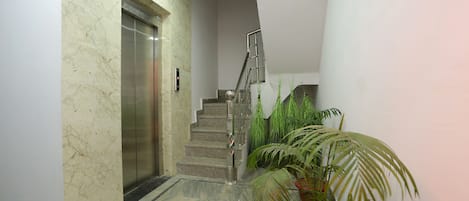 A marble-floored hallway with an elevator and a staircase leading to a landing.