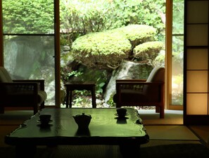 A traditional Japanese room with tatami flooring, a low table with a tea set, and a view of a lush garden through large windows. - Nanjo Ryokan (Ueda)