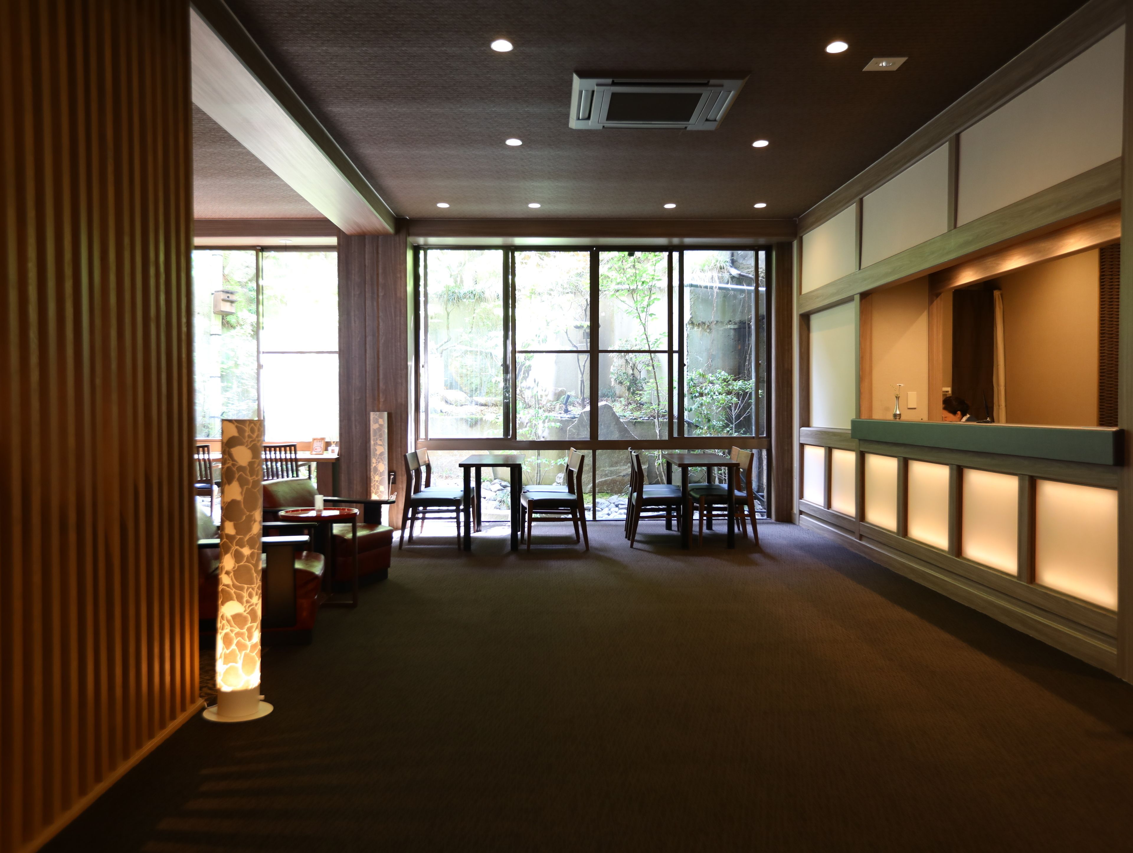 A spacious room with large windows, a reception desk, and a seating area with tables and chairs.