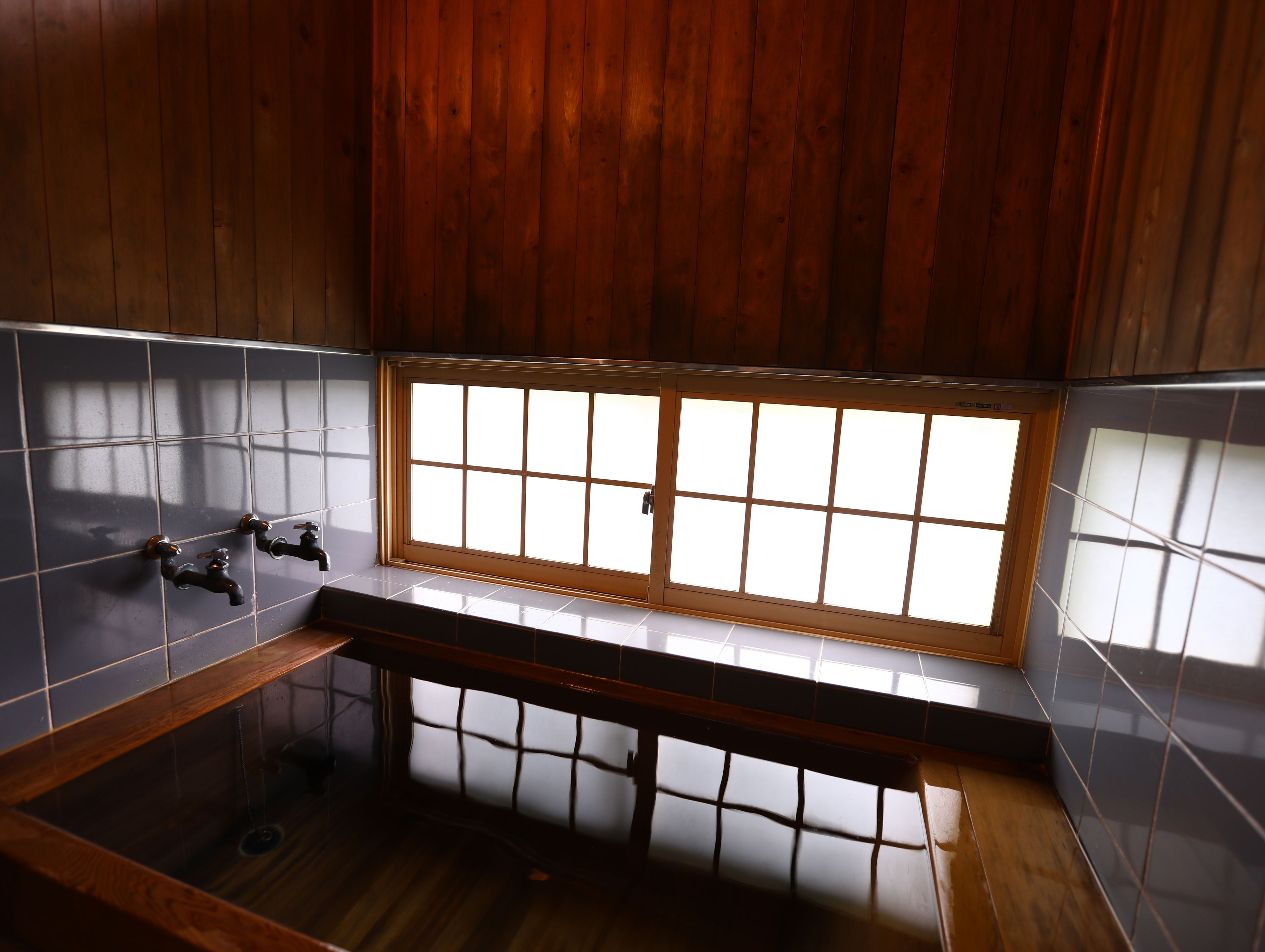 A bathroom with a wooden vanity, a bathtub, and a window with frosted glass panels.