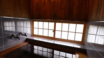 A bathroom with a wooden vanity, a bathtub, and a window with frosted glass panels.