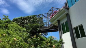 A modern building with a glass facade, a balcony with flowers, and lush greenery around. - Sabah Luxury Cozy Family Suite (Kota Kinabalu)