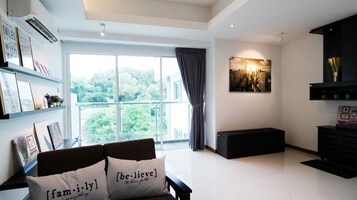 A modern living room with a large window, a sofa with decorative pillows, a black entertainment unit, and a cityscape painting on the wall.