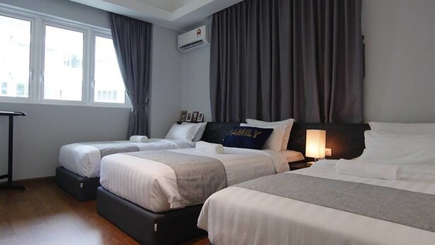 A hotel room with two beds, a bedside table with a lamp, a window with curtains, and an air conditioning unit. - Sabah Luxury Cozy Family Suite (Kota Kinabalu)