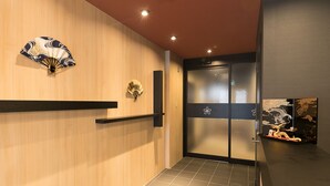 A hotel lobby with wooden paneling, a traditional fan, a decorative fan, and a glass door with a dragon design. - Stay SAKURA Kyoto Ryu (Kyoto)