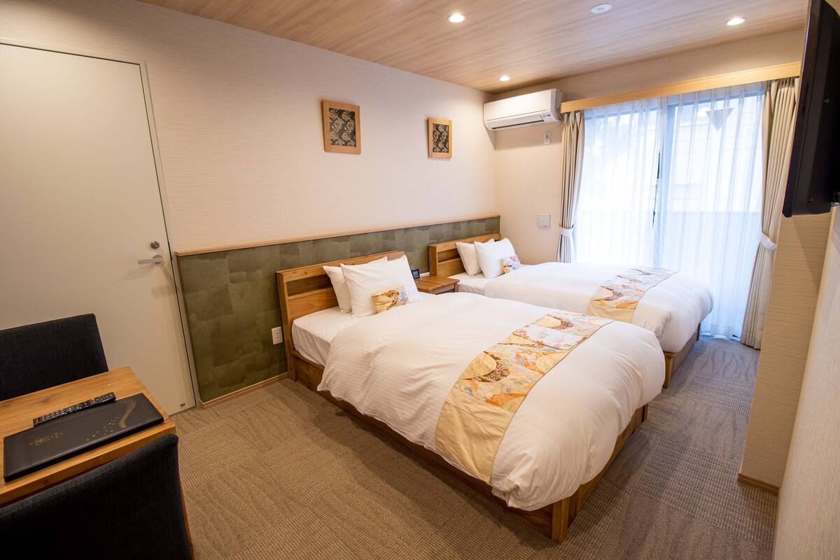 A hotel room with two beds, a desk with a laptop, and a TV.