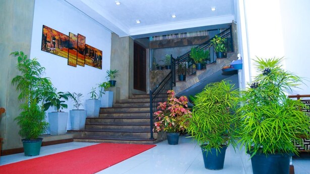 Um hall de hotel com escada, plantas em vasos e tapete vermelho.