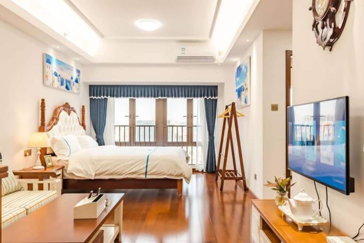 A hotel room with a large bed, a desk, a TV, and a window with curtains.