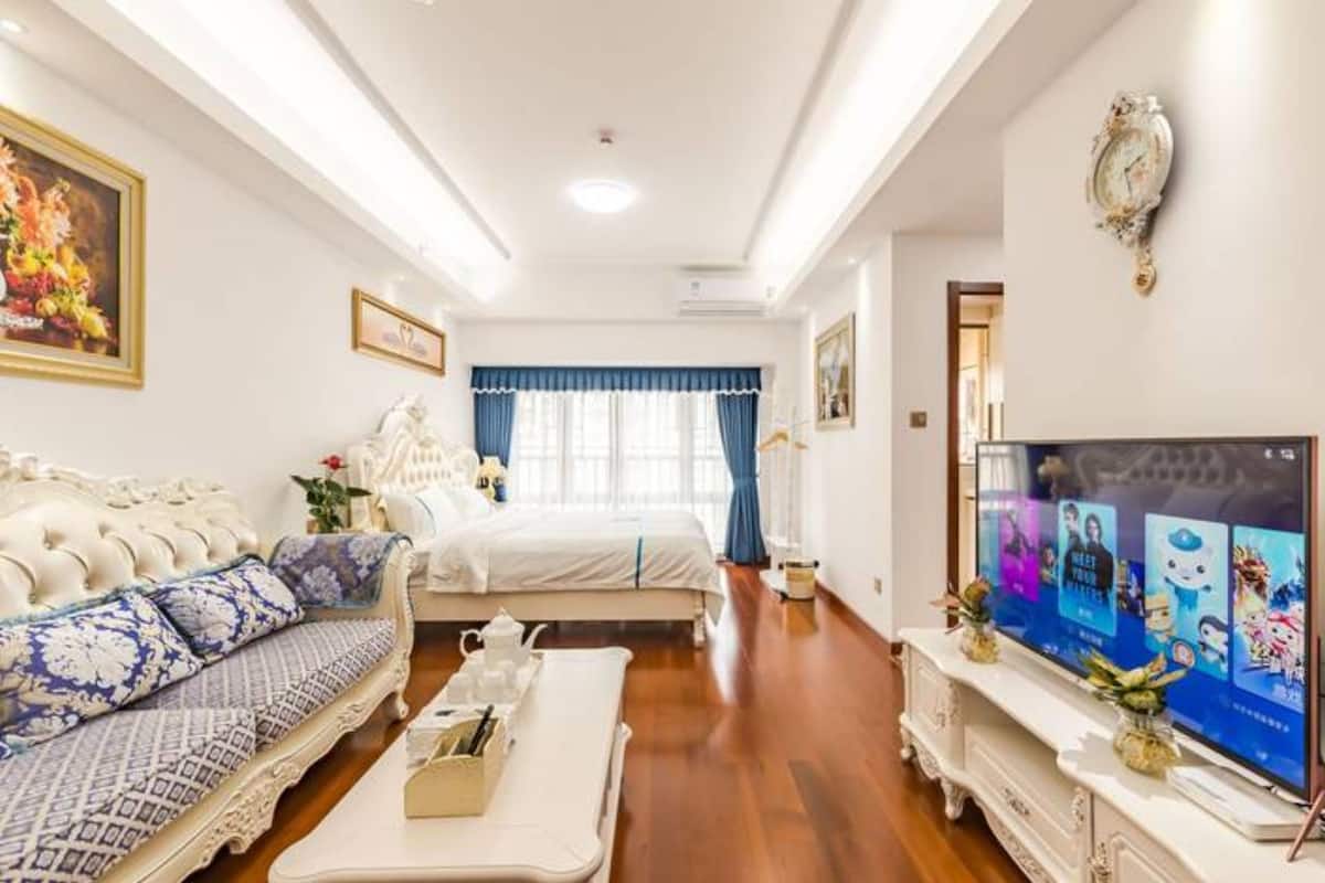 A spacious room with a large bed, a sofa, a television, and a decorative clock on the wall.