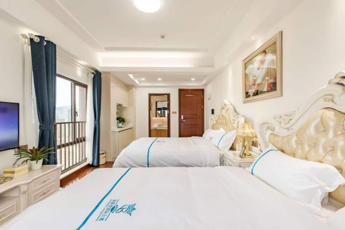 A hotel room with two beds, a TV, a desk, and a window with curtains.