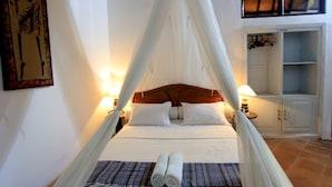 A bed with a canopy, two pillows, a rolled towel, and a bedside table with a lamp. - Alamanda (Pecatu)