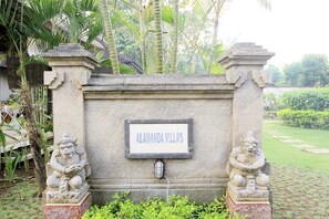 Alamanda Villa's entrance features a stone sign and flanking statues in a beautifully landscaped garden.