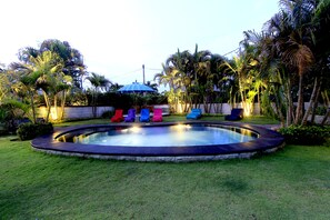 Relax by the serene pool surrounded by lush greenery and palm trees.