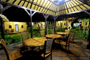 Enjoy dining under a shaded pergola with round wooden tables and comfortable seating.