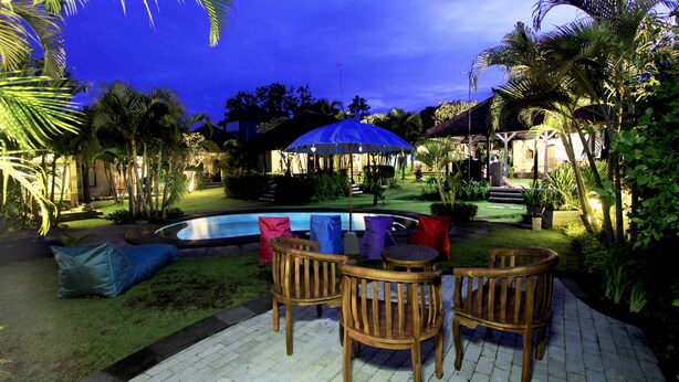 An outdoor patio with a pool, wooden chairs, and a blue umbrella. - Alamanda (Pecatu)