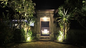 A nighttime entrance to a building with a tiled pathway leading to a door with a sign above it. - Alamanda (Pecatu)