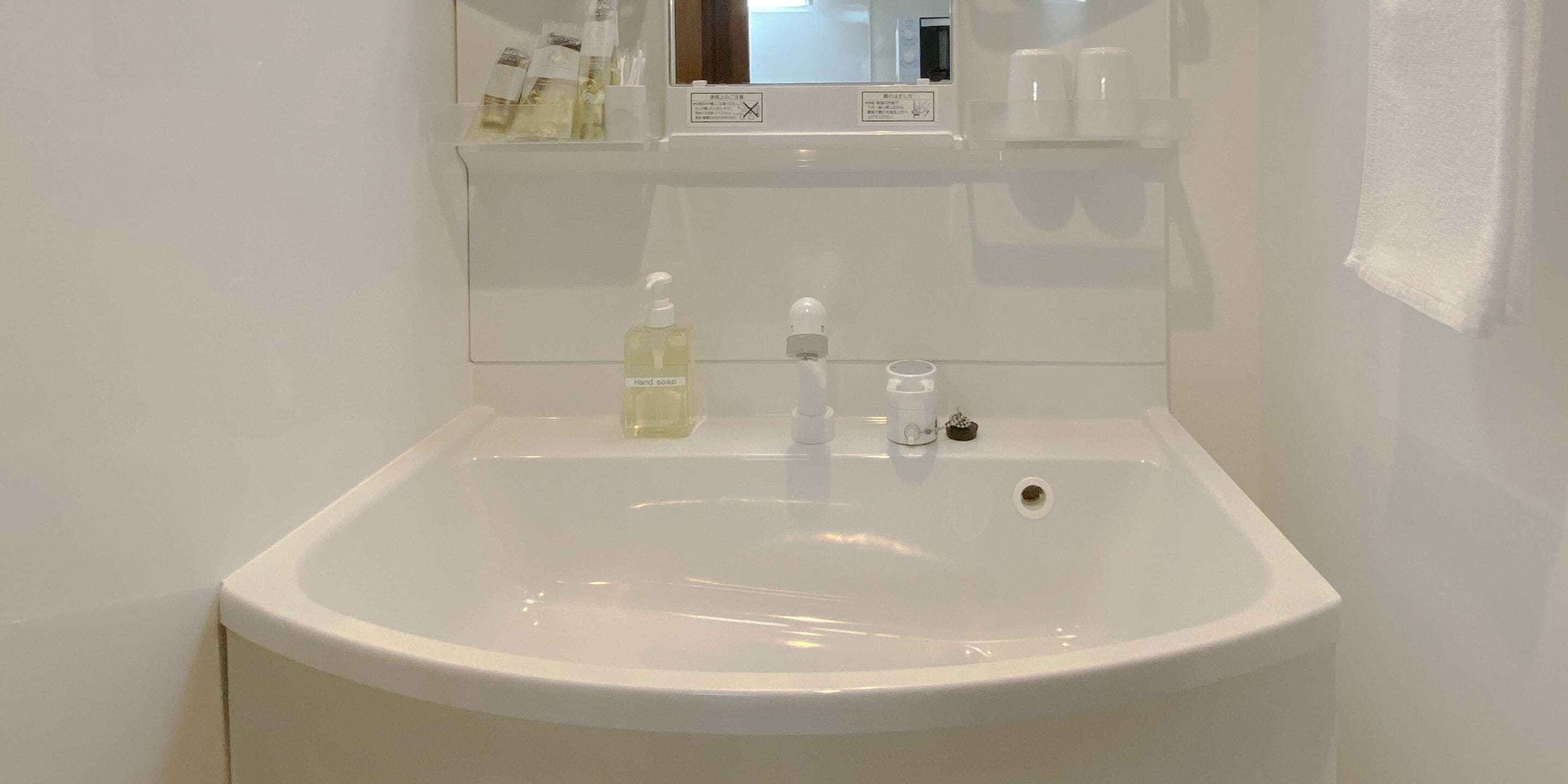A white bathroom sink with a mirror above it, a soap dispenser, and a small bottle of hand soap.