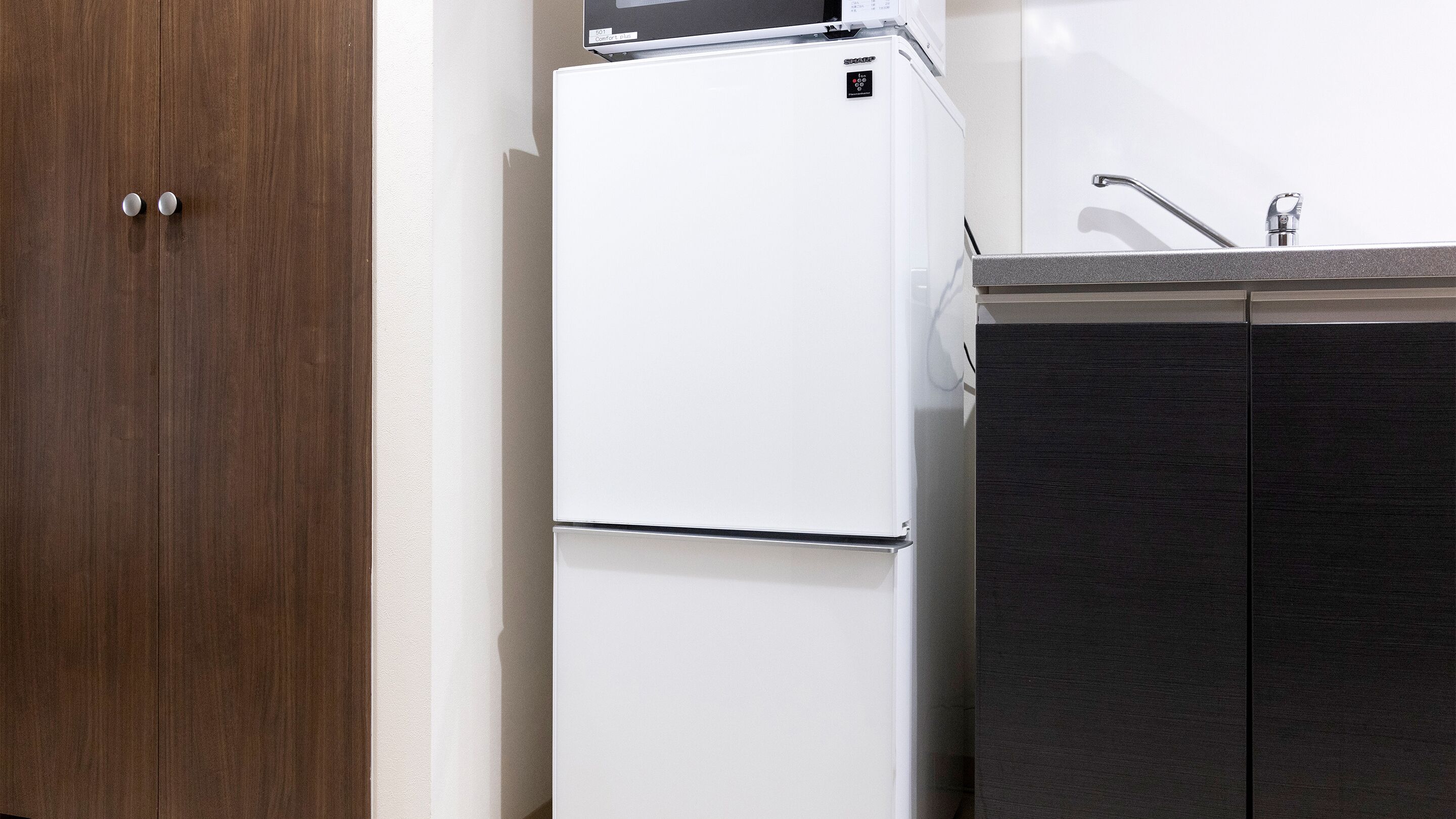 A kitchen with a white refrigerator, a wooden door, and dark cabinets.