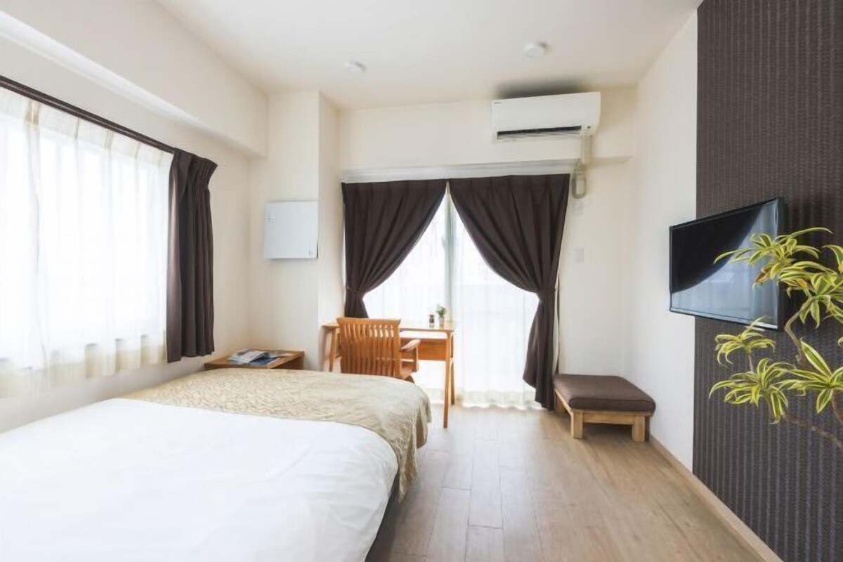 Una habitación de hotel con cama, escritorio, silla, televisión y planta.