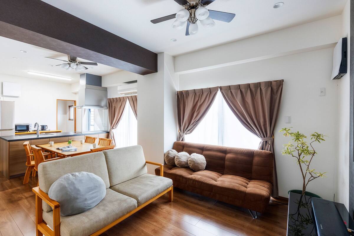 A modern living room with a sofa, a dining table, and a kitchen area in the background.